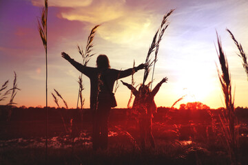 Child girl with mother in the meadow with raised hands, rear view. Relaxing. Summer sunset....
