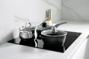 The saucepans stand on an electric induction stove. Modern modernized kitchen in the style of minimalism. Kitchen interior - obrazy, fototapety, plakaty