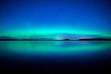 Fototapeta na wymiar Northern lights dancing over calm lake in north of Sweden