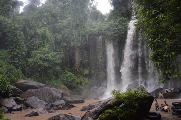 Roaring waterfall flowing into a muddy river in the jungles of Siem Reap, Cambodia, with crowds of...