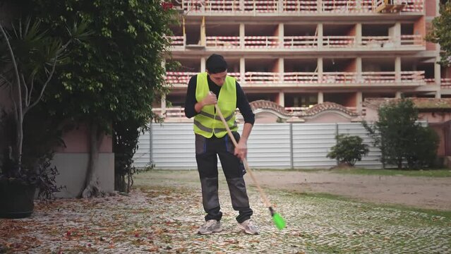 Street cleaner sweep old dry leaves city road asphalt. Sweeper man service. Janitor clean sidewalk. Urban worker care park. Young adult guy work outdoor. Person hold cleanup broom stick. Outside job.