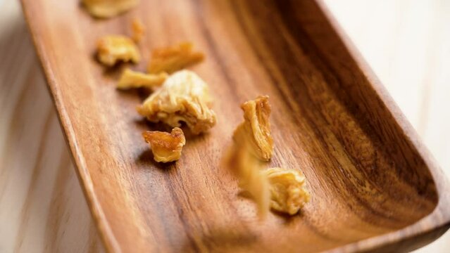 Sweet dried pineapple slices falling on a wooden bowl close up. Healthy fruity natural ingredients