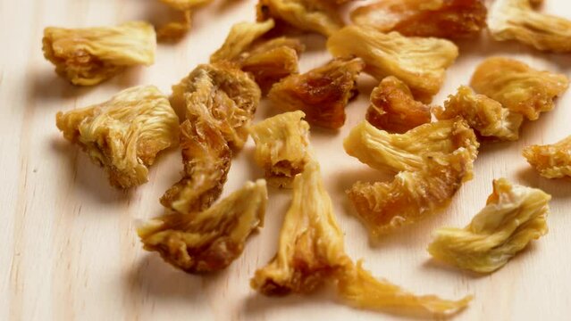 Dried dehydrated pineapple chunks on a wooden board close up. Dry ananas pieces. Rotation