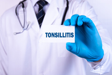 A doctor in medical clothing puts a card with the text TONSILLITIS. Medical concept.