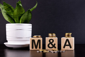 M and A or Merger and Acquisition text written on a wooden cubes with coins.