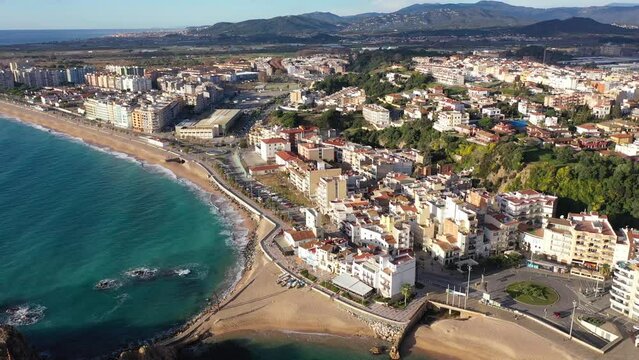 Picturesque drone view of coastal Spanish town of Blanes on bank of Mediterranean coast overlooking port, large sandy beach and Sa Palomera Rock on sunny day, Girona province, Catalonia. High quality