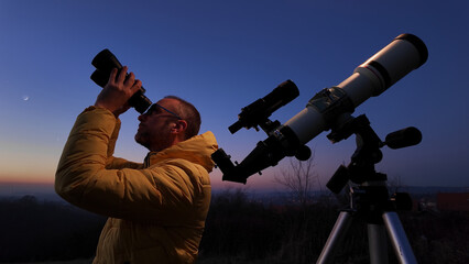 Amateur astronomer looking at the evening skies, observing planets, stars, Moon and other celestial objects with binoculars and telescope.