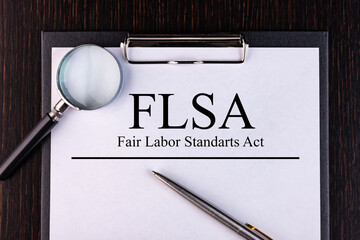 Text FLSA is written on a notebook with a pen and a magnifying glass lying on the table. Business...