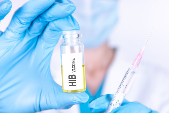 Text HIB VACCINE of is written on a bottle with the background of a doctor with a syringe in a medical glove and mask. Medical concept.