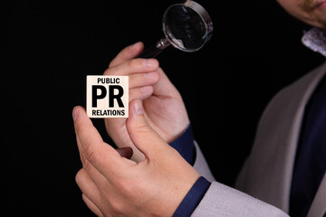 Businessman, journalist, manager holds a cube with the text PR Public Relations and looks at it...