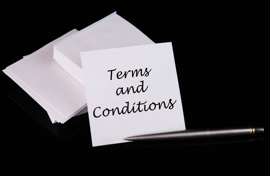 Conceptual hand writing Terms and Conditions message on a white sticker with pen on a black table.