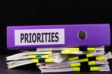 Text Priorities is written on a folder lying on a stack of papers on a table. Business concept