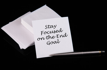 Conceptual hand writing STAY FOCUSED ON THE END GOAL message on a white sticker with pen on a black table.