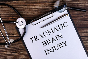 TRAUMATIC BRAIN INJURY text is written on a tablet lying on a dark table with a stethoscope and a...