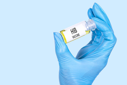 HIB VACCINE text is written on a vial whose ampoule is held by a hand in a medical disposable glove. Medical concept.