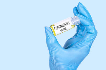 CORONAVIRUS VACCINE text is written on a vial whose ampoule is held by a hand in a medical...
