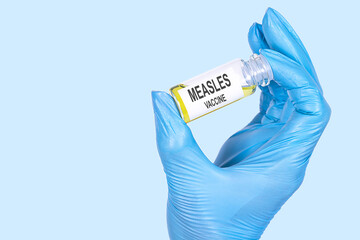 MEASLES VACCINE text is written on a vial whose ampoule is held by a hand in a medical disposable glove. Medical concept.