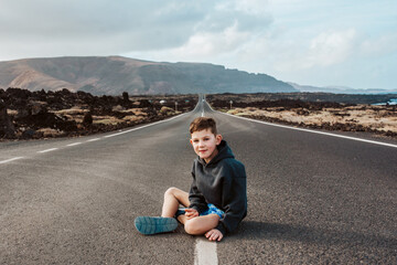 Portrait of boy sitting on empty road.