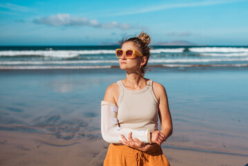 Woman with broken arm on beach. Arm cast, injured during family vacation in holiday resort. Concept of beach summer vacation. - obrazy, fototapety, plakaty
