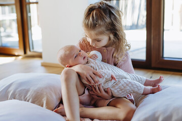 Portrait of big sister holding newborn sister. Girl carefully cuddling small baby. Sisterly love, joy for new family member.