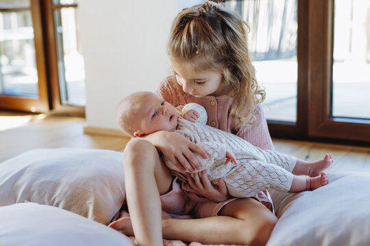 Portrait of big sister holding newborn sister. Girl carefully cuddling small baby. Sisterly love, joy for new family member.