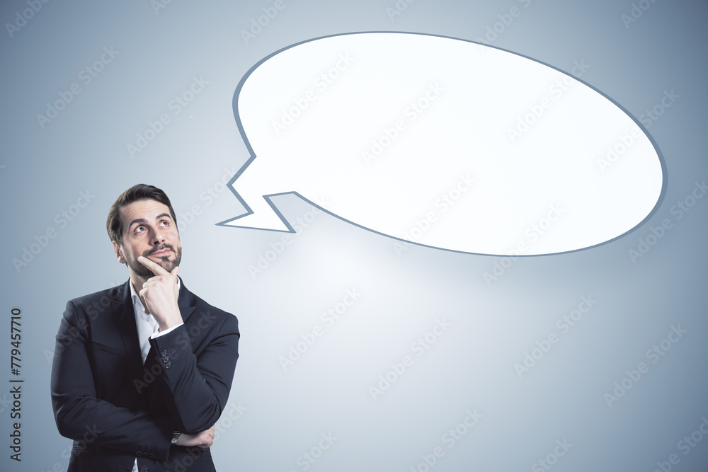 Poster thoughtful young businessman with empty speech bubble on gray background. opinion and mock up place.
