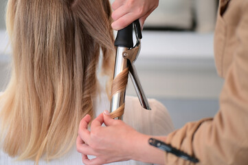 Hair iron or straightener used by a hairdresser for curly hair of a blonde client