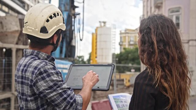 Engineer constructor discuss build plan with investor woman. Builder guy show construction site project tablet pad. Worker tell blueprint client. Man work city street Customer look at new house scheme