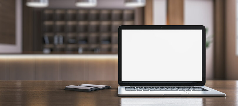 Close up of creative wide designer desk with empty white laptop and blurry office in the background. Mock up, 3D Rendering.