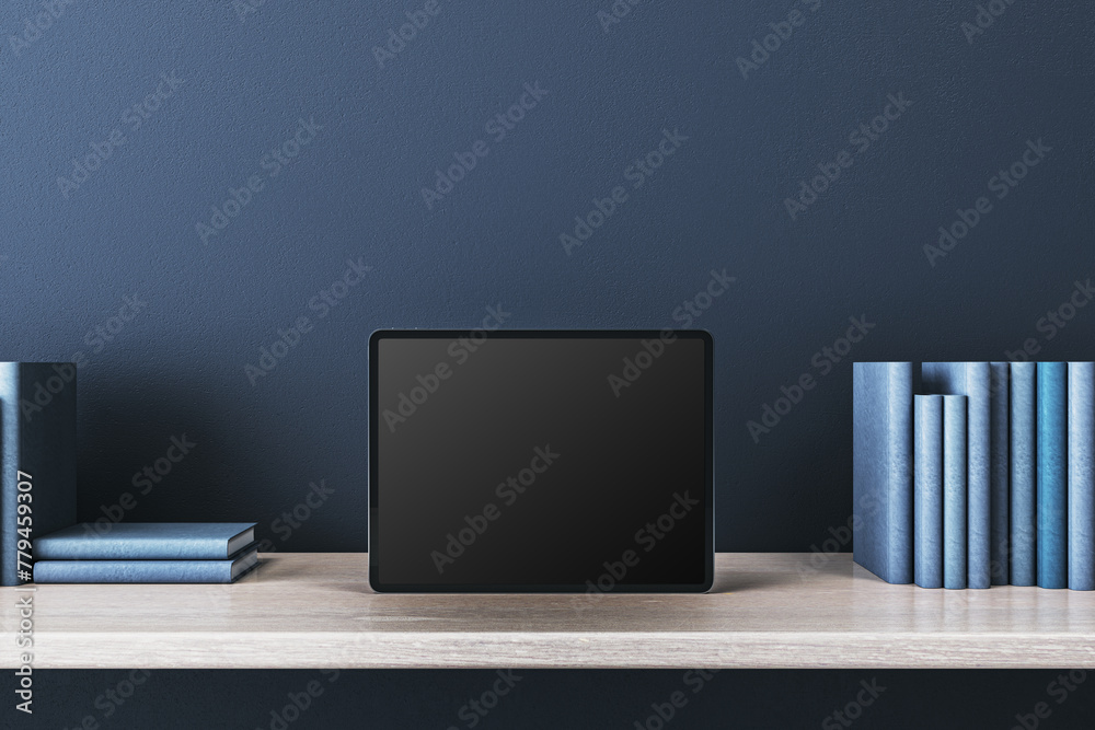 Poster close up of creative wooden designer desk with books and empty mock up tablet on blue concrete wall.