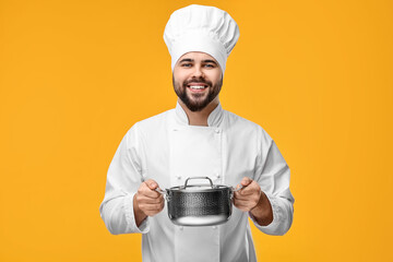 Happy young chef in uniform holding cooking pot on orange background