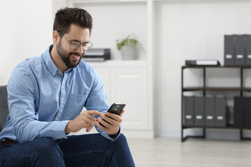 Handsome young man using smartphone in office, space for text