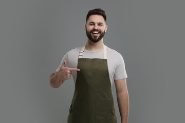 Smiling man pointing at kitchen apron on grey background. Mockup for design