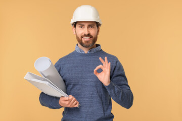 Architect in hard hat with draft and folder showing OK gesture on beige background