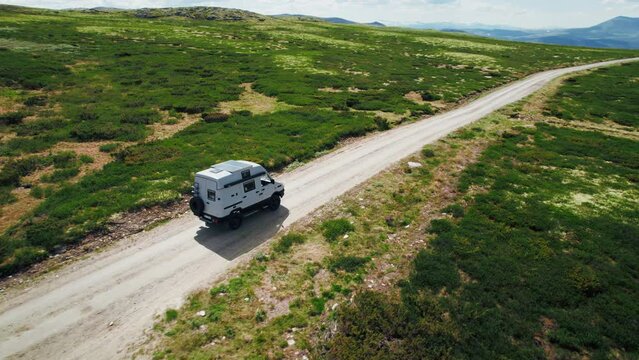 Aerial shot of cool overland car, adventure off-road camper van drive on gravel secluded remote road on mountain terrain. Solar panel on roof rack for off-grid living and travel