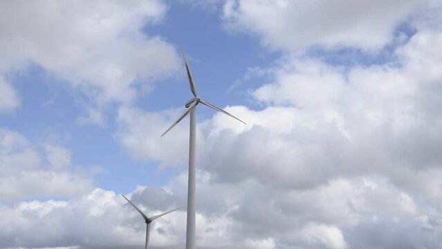 The white blades of two wind turbines rotate against a background of blue sky with clouds.