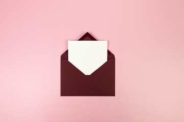 Top view of dark red envelope, white card on pink background. Post flat lay. Copy space.