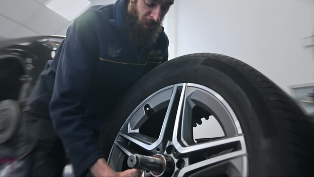 Technician work car service. Auto mechanic balancing big wheel. 30s man change tyre cover job. Guy fix tire workshop. Worker repair vehicle. Repairman person replace cast disk. Engineer blue uniform.