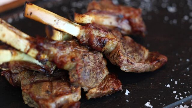 Lamb chops. 4K close up video with some lamb chops grilled on barbecue and placed on a black plate with salt next to it. Rotating table. Lamp grill cooking.