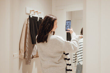 Korean teenage girl takes a selfie in new clothes in the mirror and sends it to her friend via phone in a shopping mall. Retail and consumerism. Sale promotion and shopping concept. Part of a series - 779468754