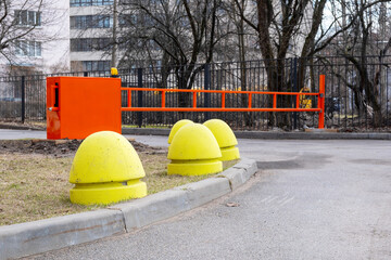 Yellow concrete hemispheres on the grass lawn and a closed automatic barrier