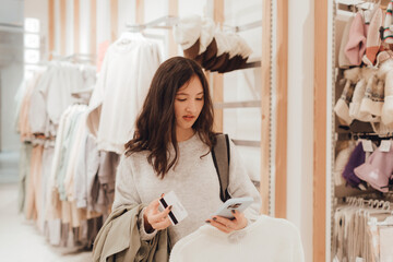 Korean teenage girl holds a credit card in her hands and wants to pay for new clothes in a shopping mall. Retail and consumerism. Sale promotion and shopping concept. Part of a series - 779471792