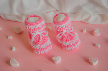 Pink knitted booties on pink background with marshmallow hearts