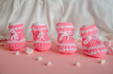 Pink knitted booties on pink background with marshmallow hearts