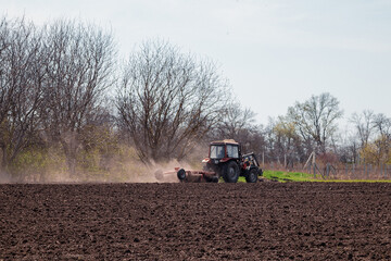 Obraz premium A farmer on a tractor prepares the land with a cultivator for sowing seeds. Agriculture, farming.