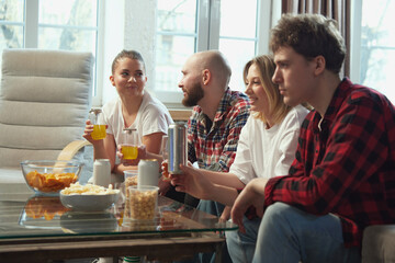 Fototapeta na wymiar Happy, positive young people friends sitting on sofa at home, eating snacks, chips and lively discussing football match translation. Concept of sport, championship, leisure and entertainment