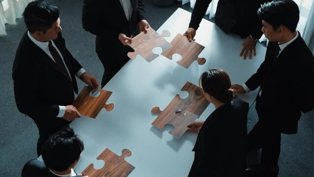 Top view of business people putting jigsaw together at meeting room. Professional marketing team standing at table while gathering puzzle piece. Show unity, cooperation and team working. Directorate.