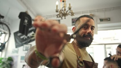 Brutal young adult man work cozy barbershop. Cool barber show scissors close up. Male hairdresser closeup. Hairstylist guy look camera. 30s person hair cut retro beauty salon. Vintage haircut shop.