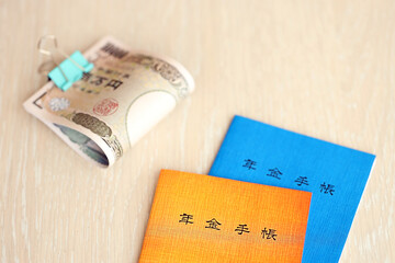 Japanese pension insurance booklets on table with yen money bills. Blue and orange books for japan pensioners close up