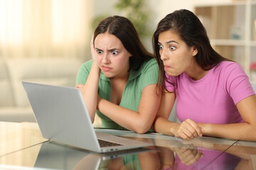 Perplexed friends watching media on laptop at home